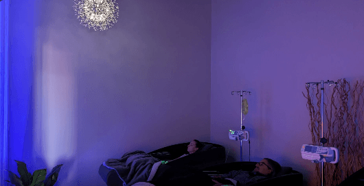 Two clients relaxing in recliners during an appointment at a softly lit local wellness lounge